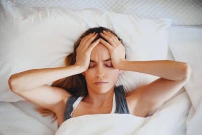 woman holding her head in pain while she lays in bed