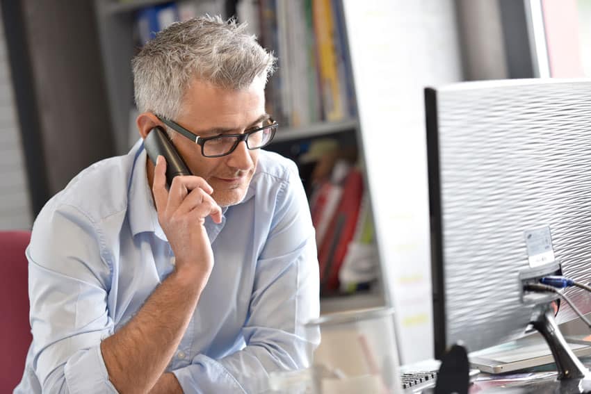 adult man sitting at work desk talking on the phone