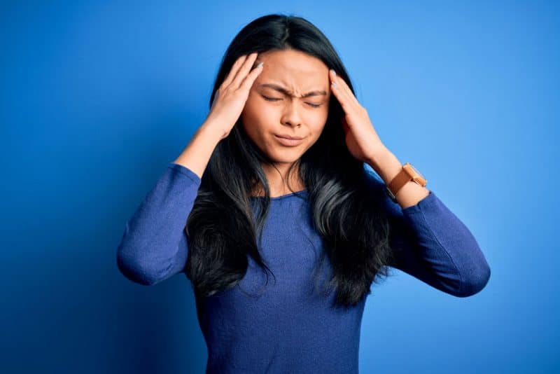 woman with blue blouse holds her head due to a holiday migraine headache