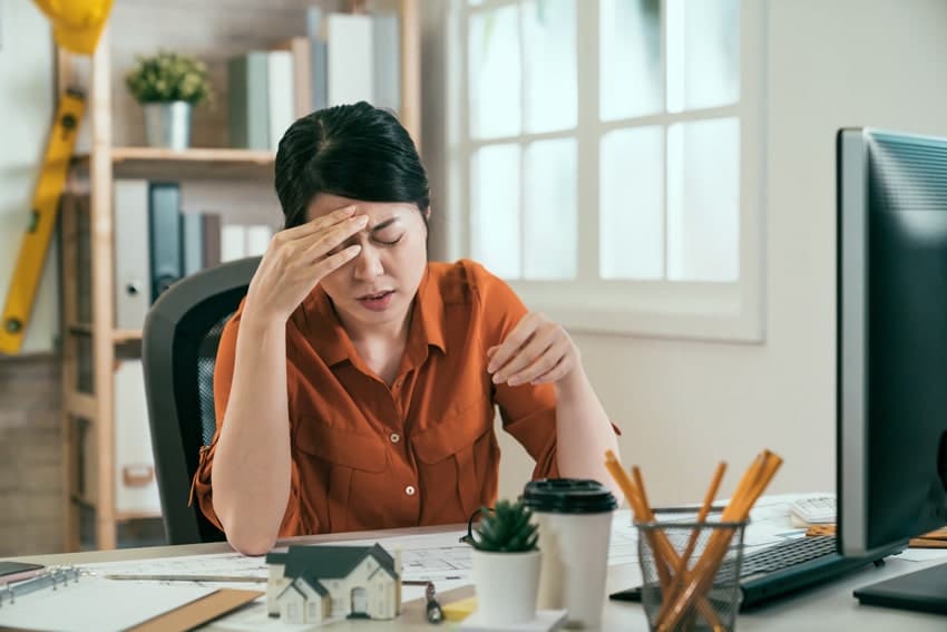 adult woman sitting at a desk and holding her head in pain